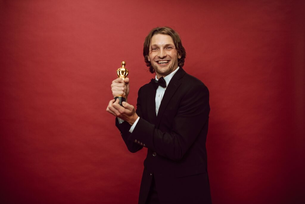 Smiling man in a tuxedo holding a trophy against a red background, celebrating success.